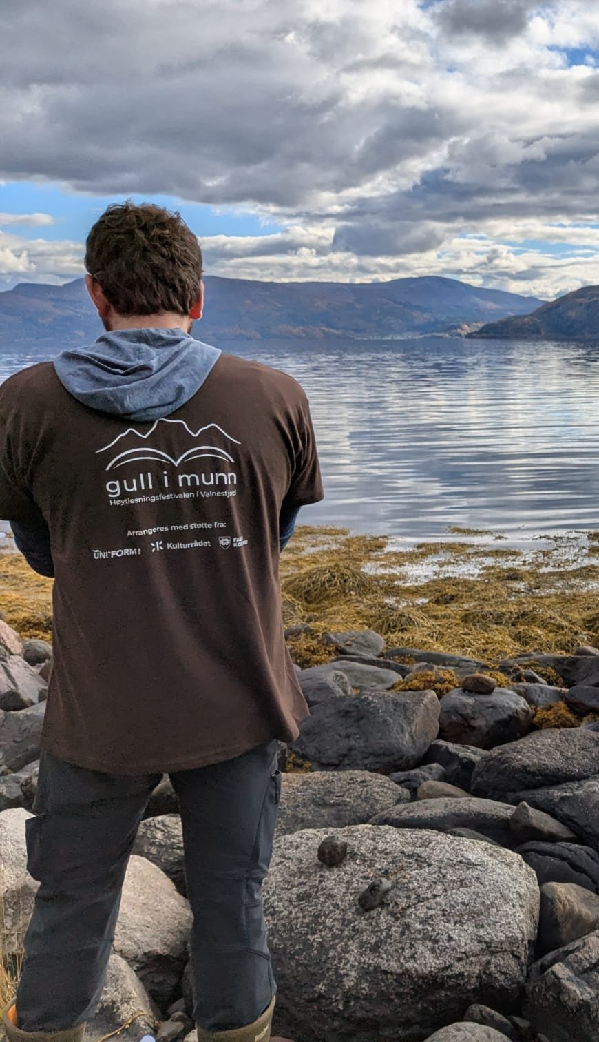 Guide in a Gull i munn festival shirt looking out over the fjord from the rocky shore